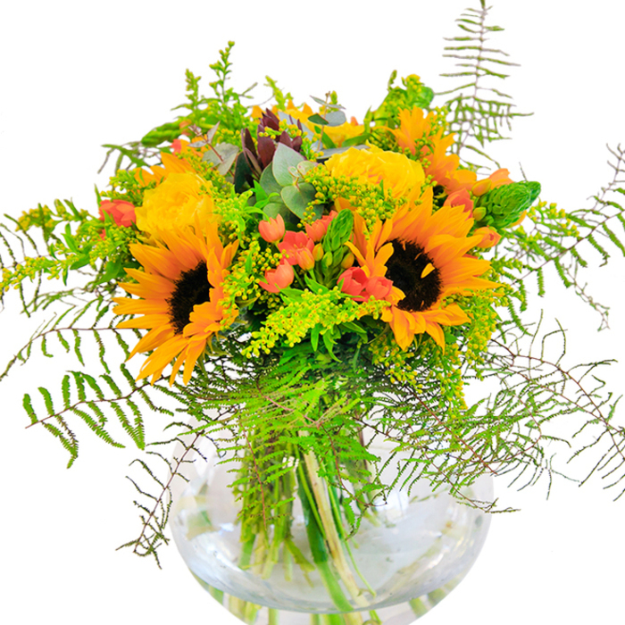This exquisite bouquet brings together the cheerfulness of yellow sunflowers and garden roses into a lively celebration, crafted with the artistry only a Tooting Bec florist can provide. Upon first glance, large sunflowers with golden petals and chocolate-brown centres stand tall, radiating warmth akin to the sun rising over Tooting Common on a clear morning. Dotted among them, yellow blooms unfurl in intricate spirals, their soft petals giving off a gentle richness. The vibrant red Hypericum berries glisten amongst lush greenery, offering a delightful contrast and depth that draws the eye and evokes the bustling vibrancy of local markets. The feathery trailing fronds and fine filler blooms-solidago perhaps, gently dusted with minute yellow florets-cascade naturally, reminiscent of the wilder patches along the edge of the Bec. Eucalyptus leaves add a muted, blue-green accent, threading a hint of woodland cool through the bold yellows and reds. The bouquet is elegantly anchored in a clear, round glass vase, reminiscent of classic flower arranging traditions, where the tangle of vibrant stems is visible beneath glimmering water. This composition seems to hum with the subtle scent of roses and sunlight, inspiring thoughts of joyous celebrations-birthdays, anniversaries, or simply a welcome for friends or family-across Tooting Bec and its nearby neighbourhoods. Each element, from petal to leaf, comes together in this arrangement to form a heartfelt ode to brightness, local pride, and floral excellence.